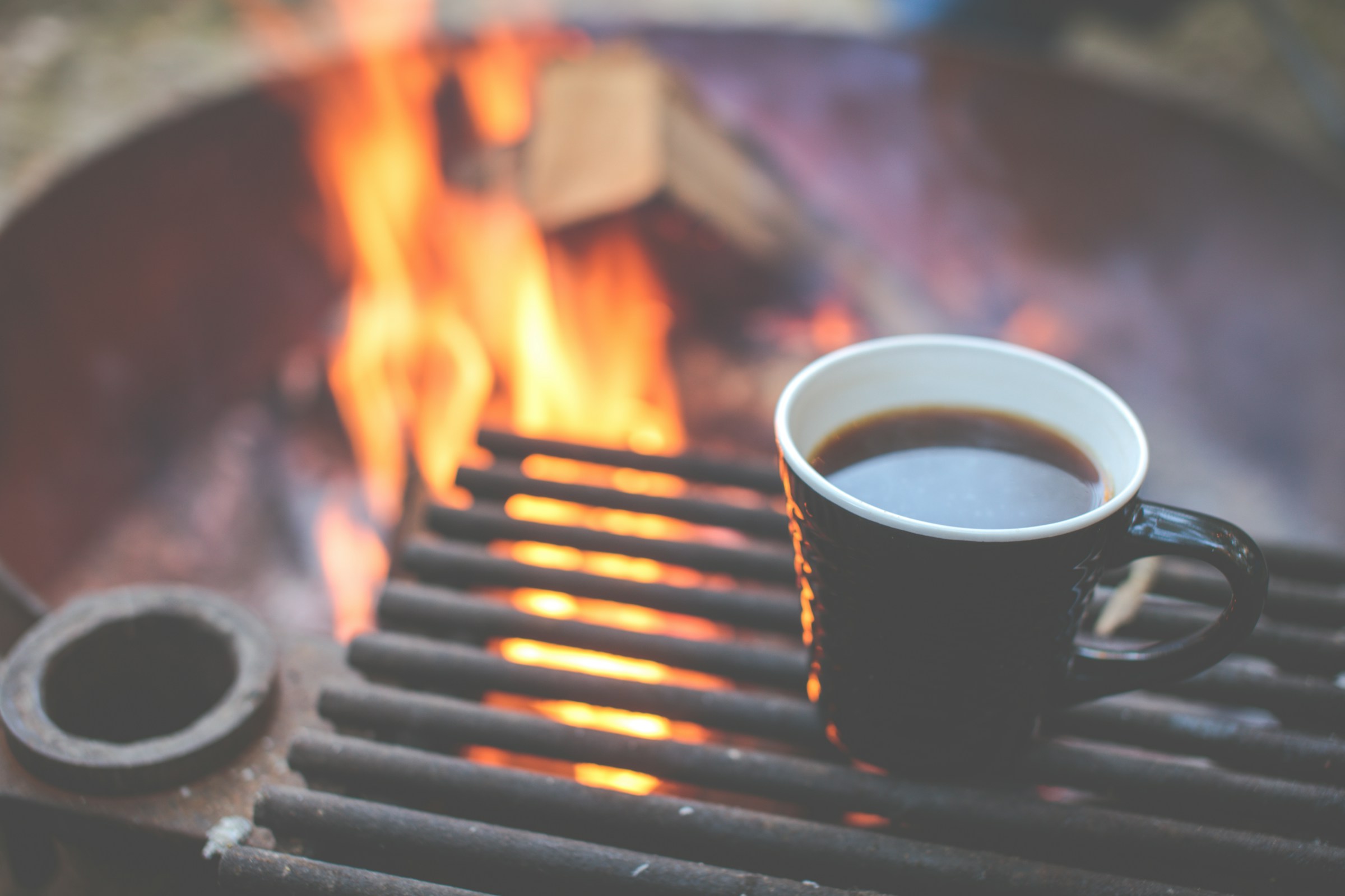 Black enamel coffee mug warming beside a crackling campfire