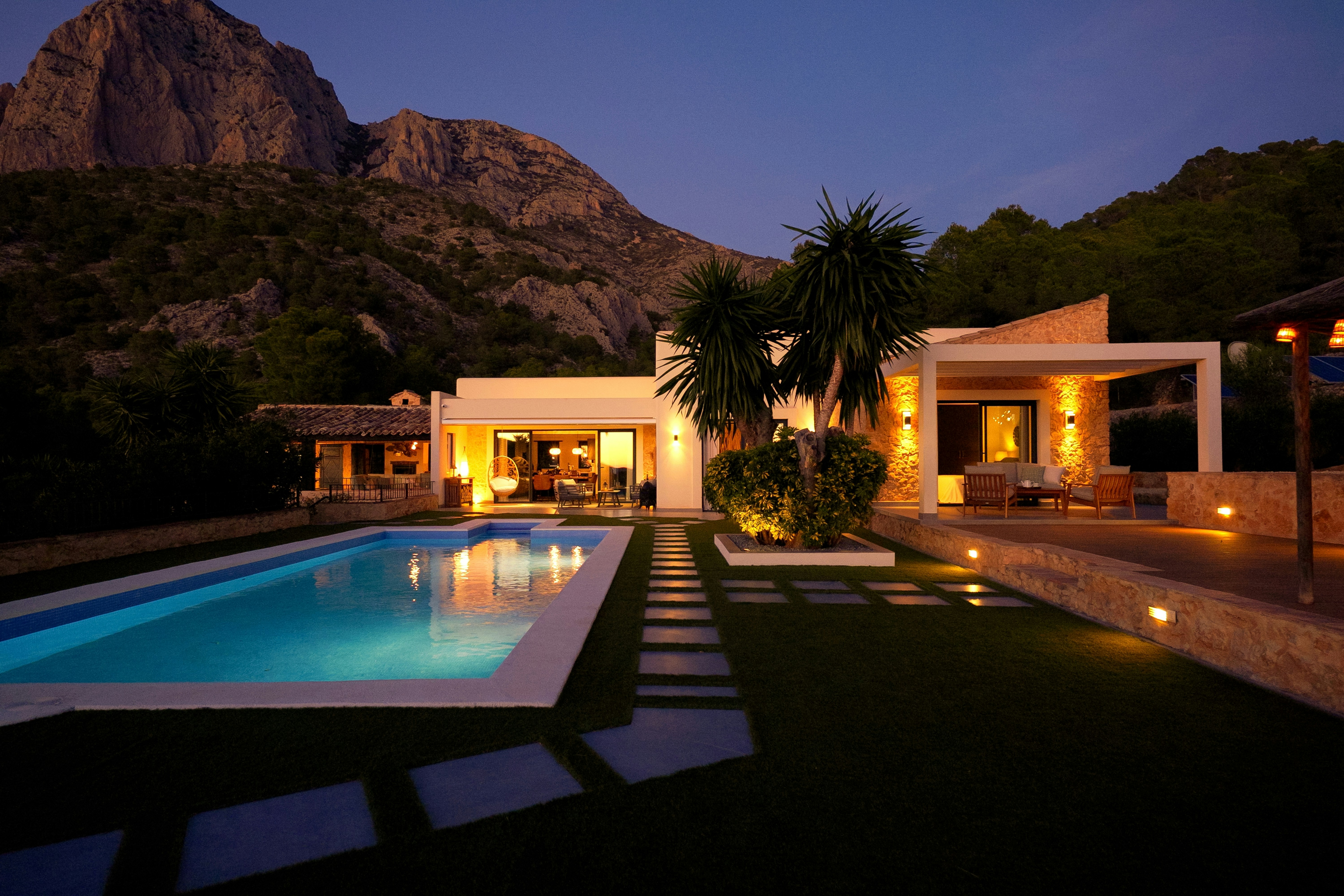 Landscape lighting illuminating a stepping-stone path beside a pool at dusk